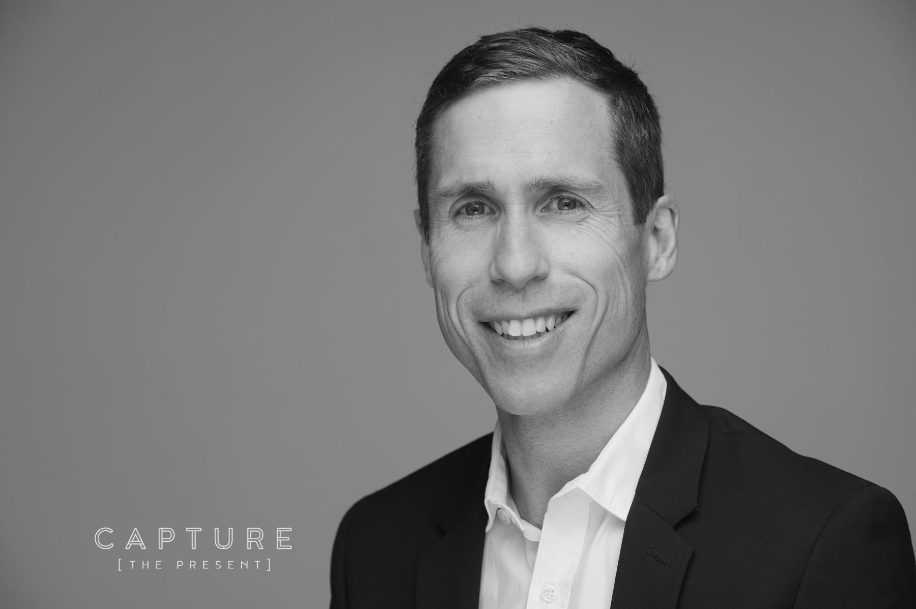 Lawyer in a dark suit smiling against a grey studio backdrop