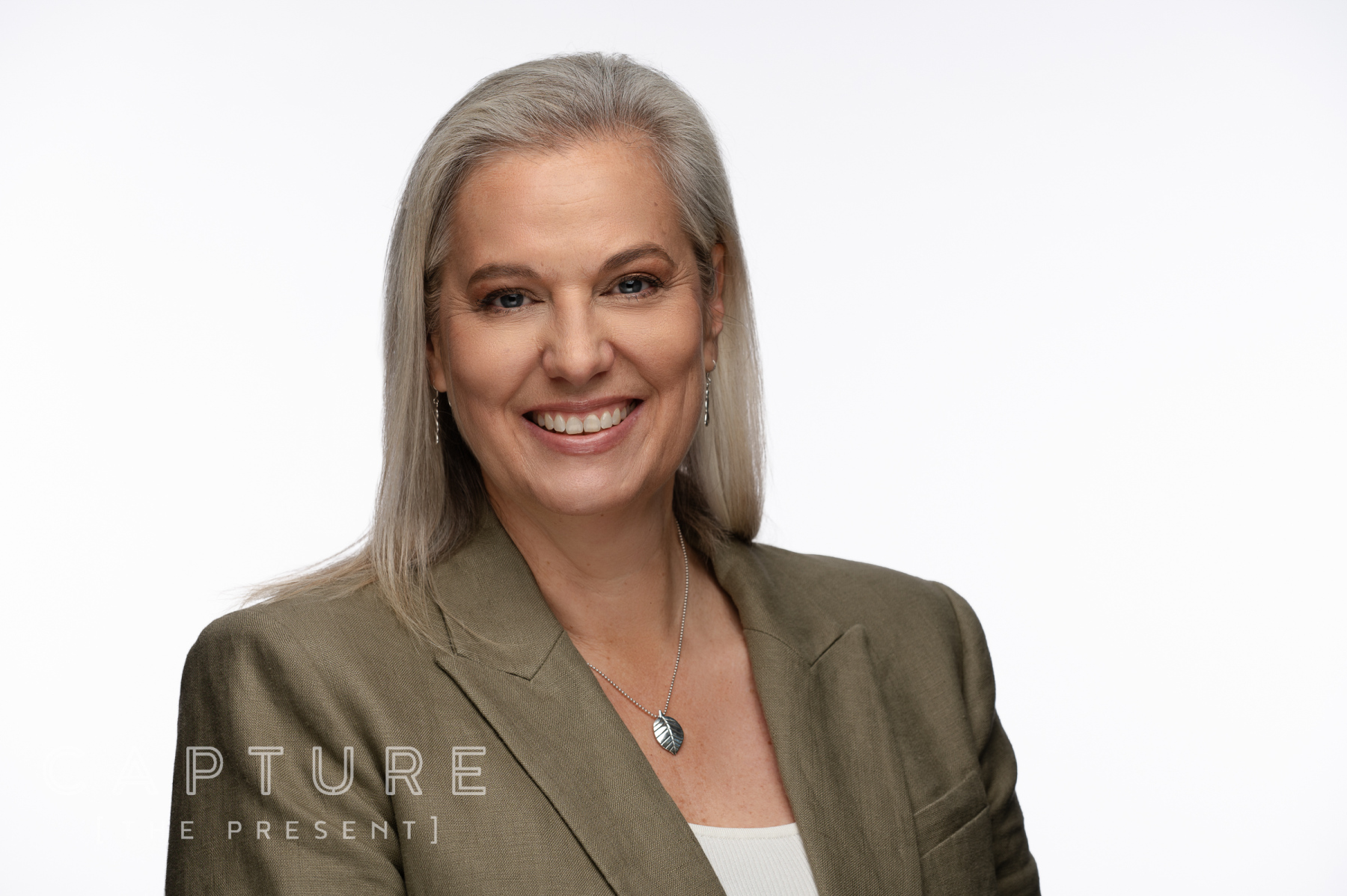 Woman in an olive blazer with a light, clean studio background