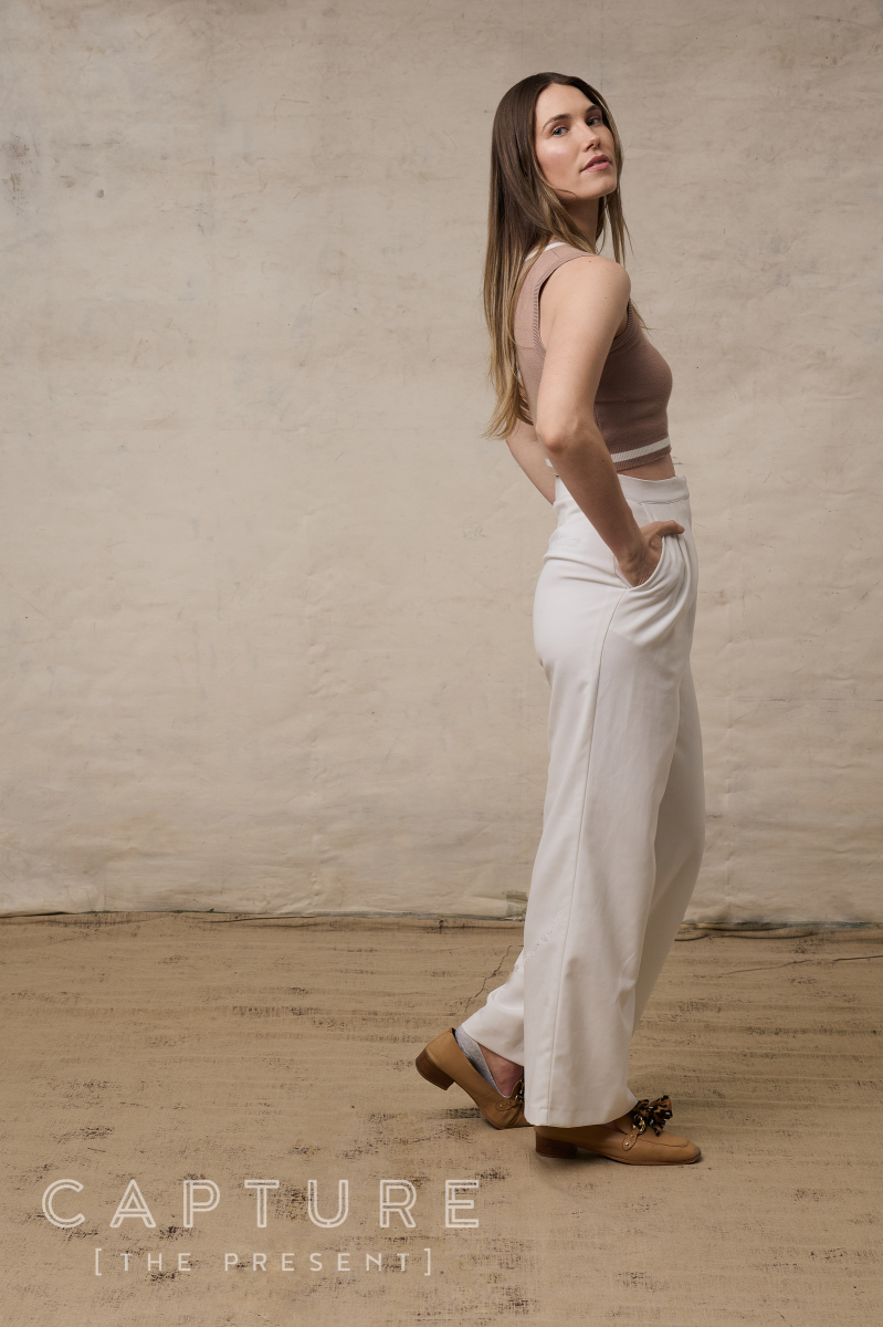 Caitlin Bahr in a cropped knit top and wide white trousers against a canvas backdrop