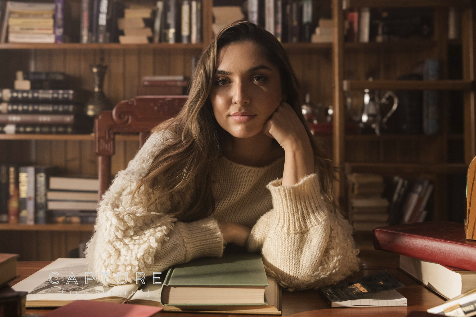 Woman in a cream knit jumper resting her chin on her hand in a private library at a residential home in Glenelg