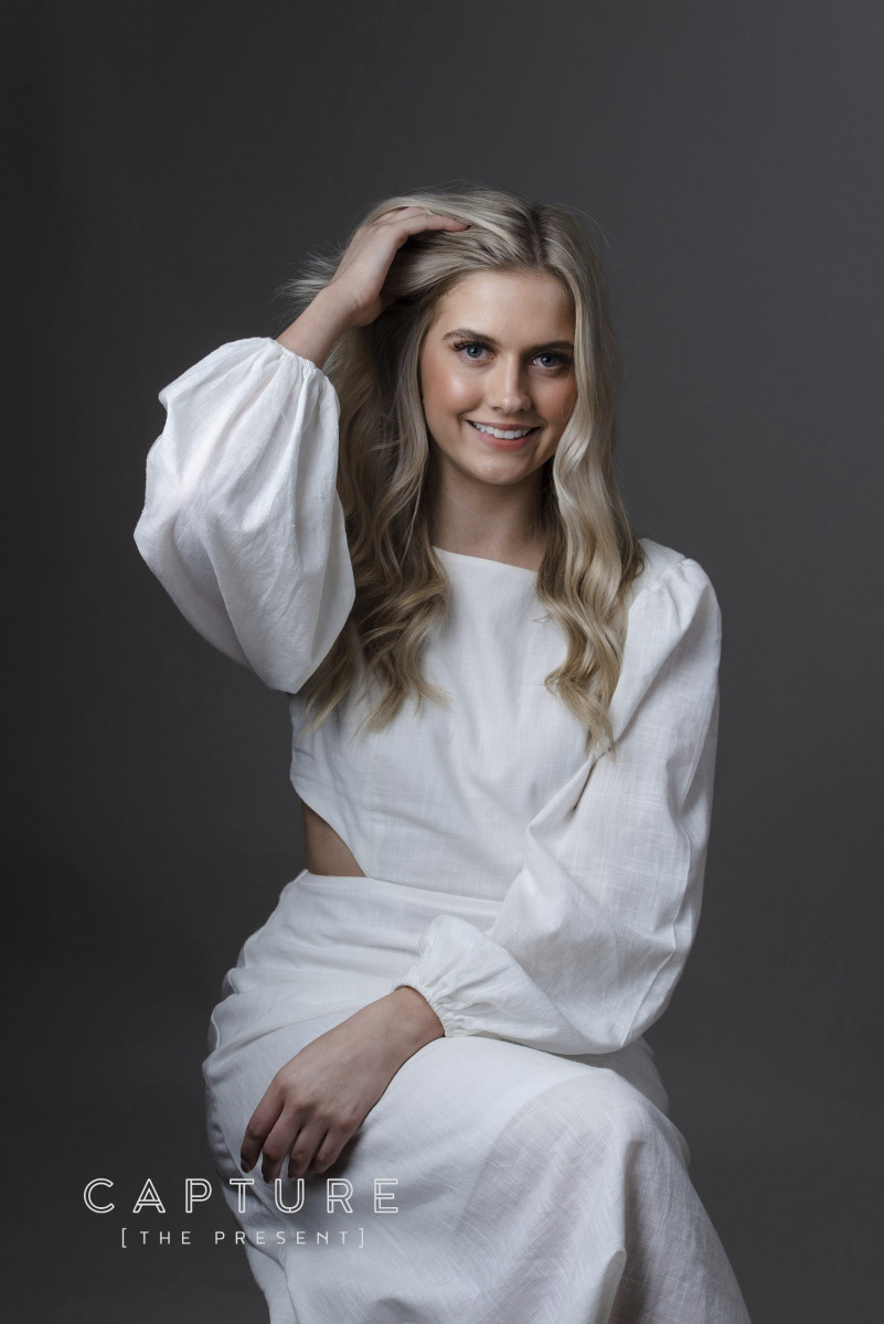 Model Mikayla in a white dress posing against a grey studio backdrop