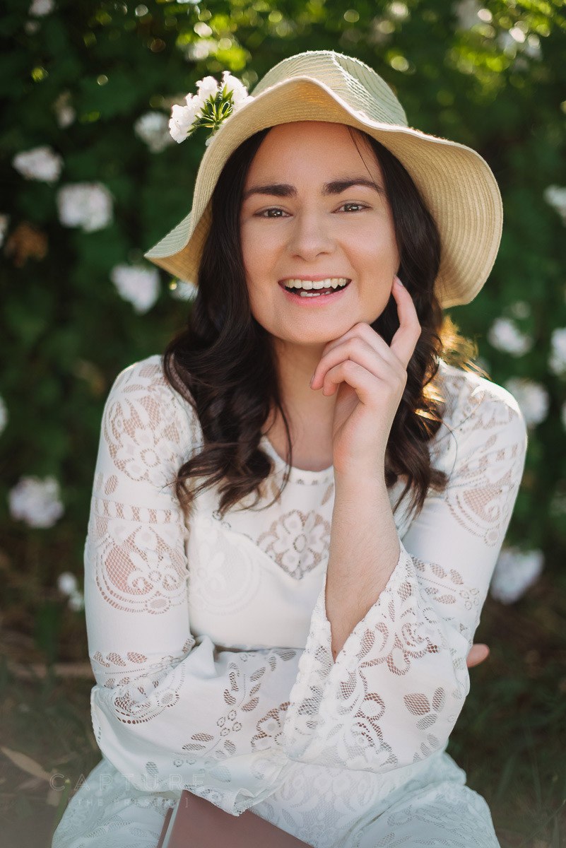 Smiling woman in a straw hat and white lace top among flowering shrubs in the Adelaide Hills