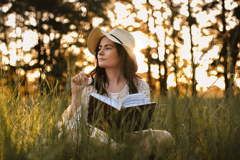 Woman in a sun hat reading a book in long grass at sunset in the Adelaide Hills