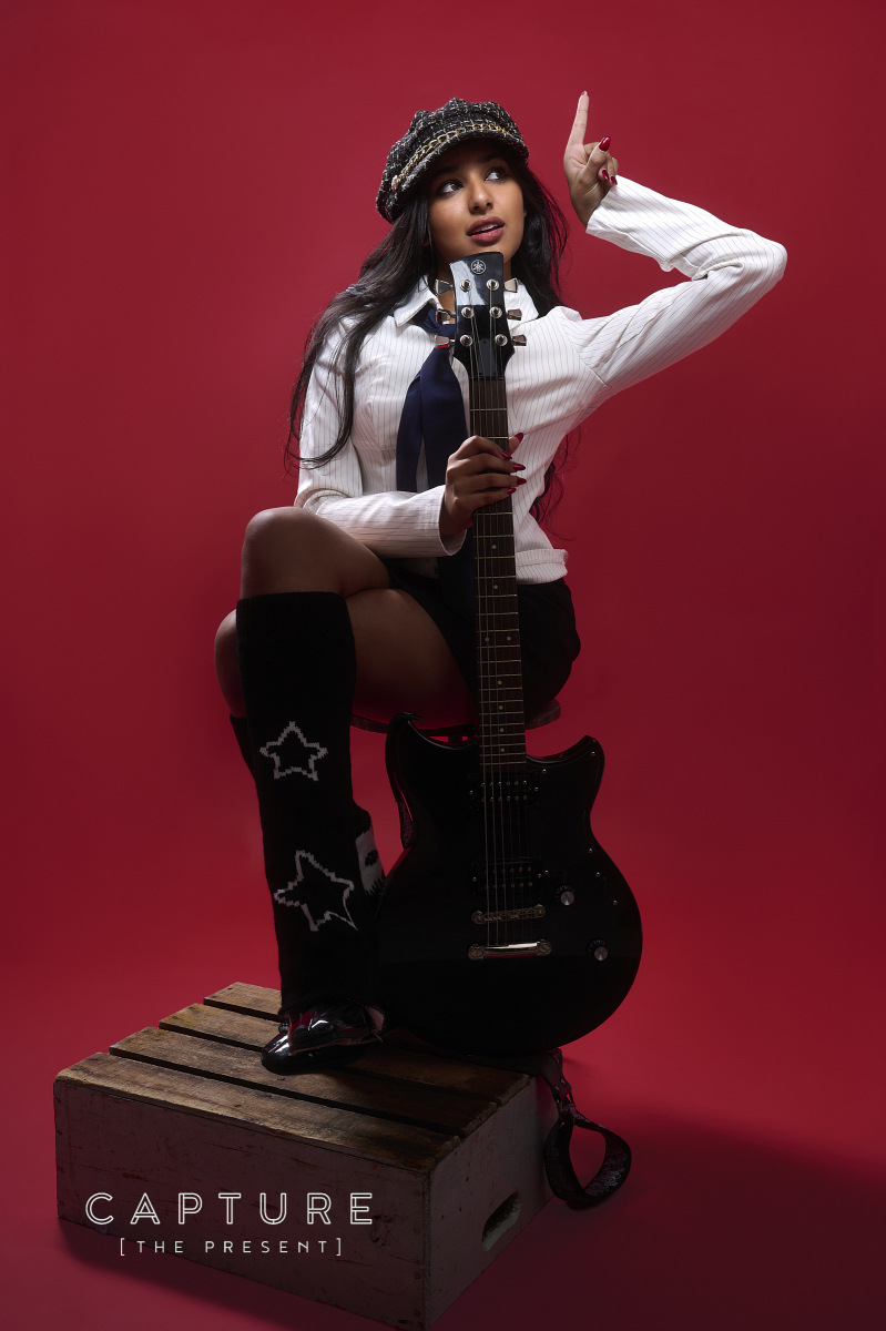 Adelaide singer Twisha seated with her guitar against a red studio backdrop at Cog Creative Space