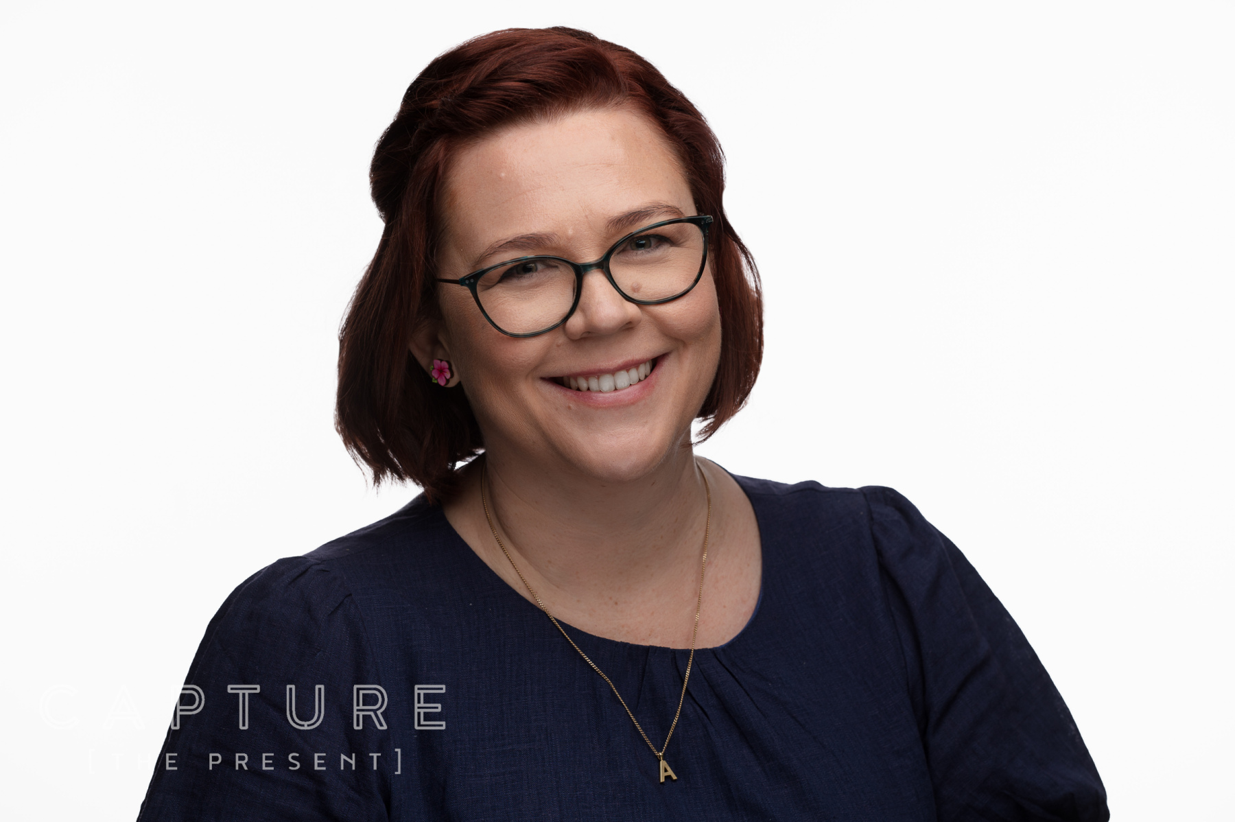 Woman with dark hair and glasses in a black top on a white backdrop