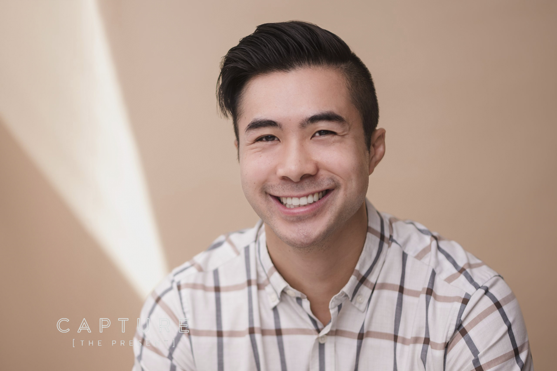 Man in a checked shirt smiling in warm studio light