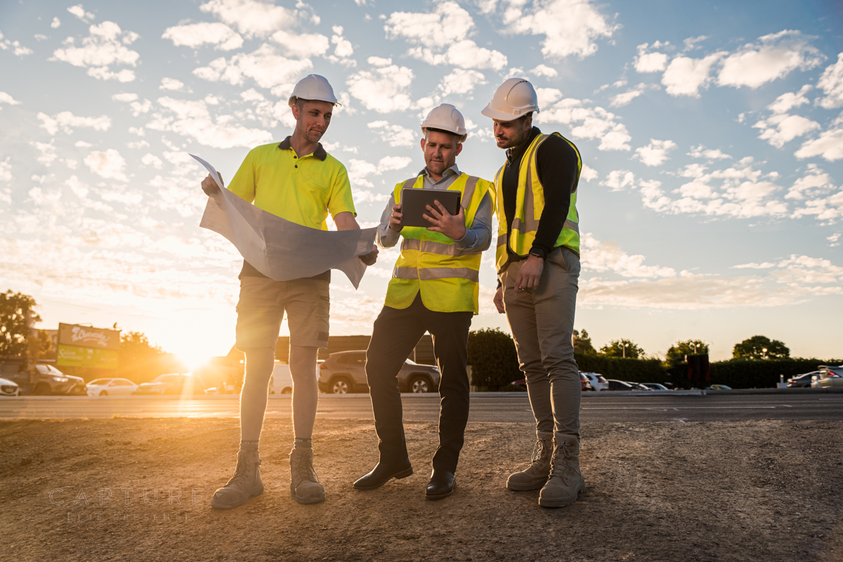 Three construction workers in hi-vis reviewing site plans at sunset