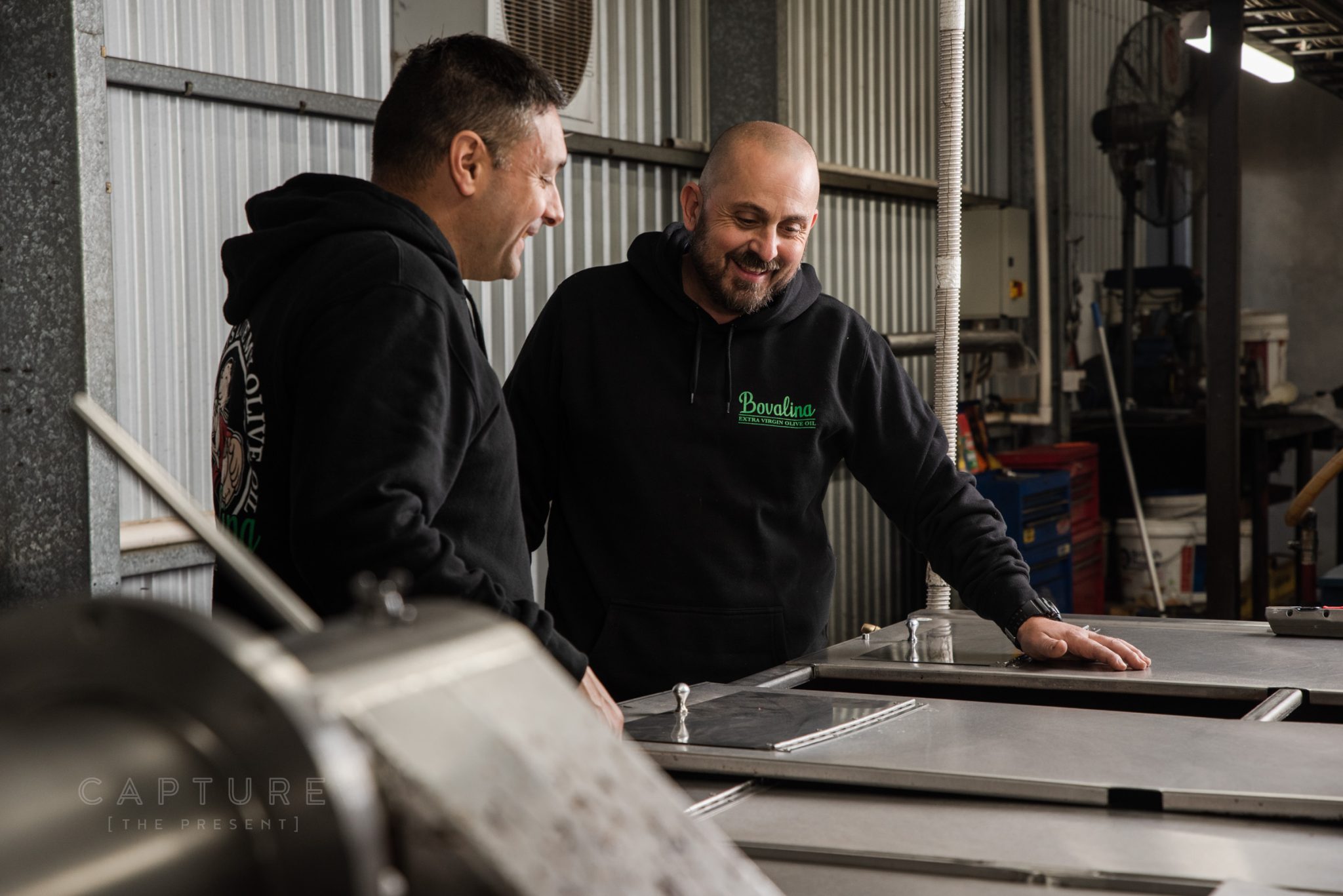 Two of the Bovalina family laughing beside the press in the processing shed