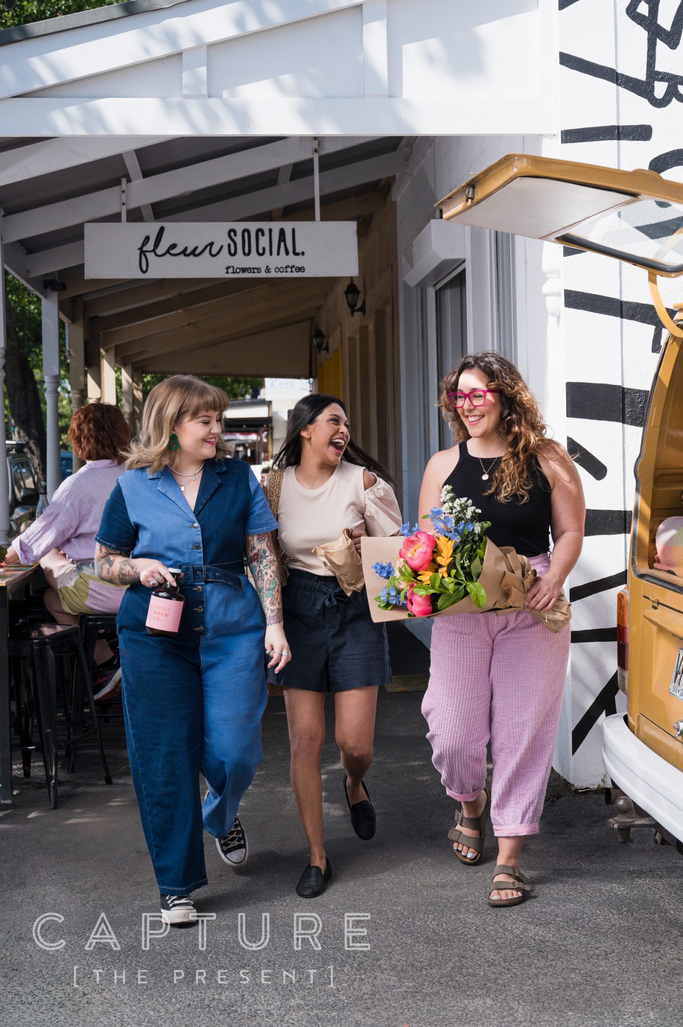 Three women laughing outdoors, one carrying flowers, in the Barossa Valley