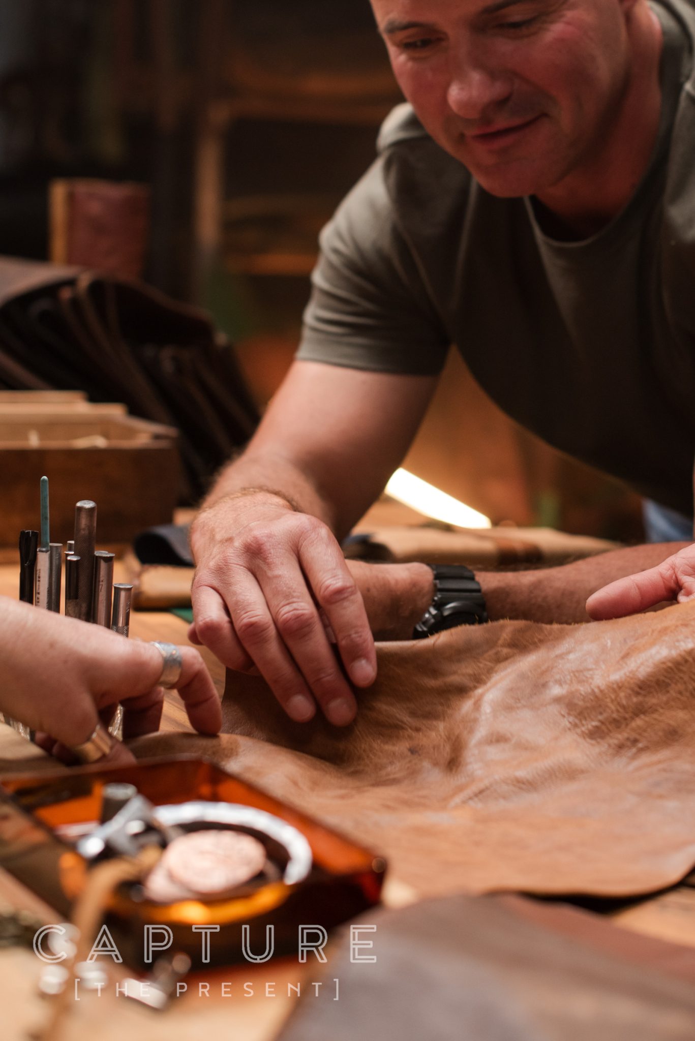 Hands cutting and shaping leather with hand tools on a workbench