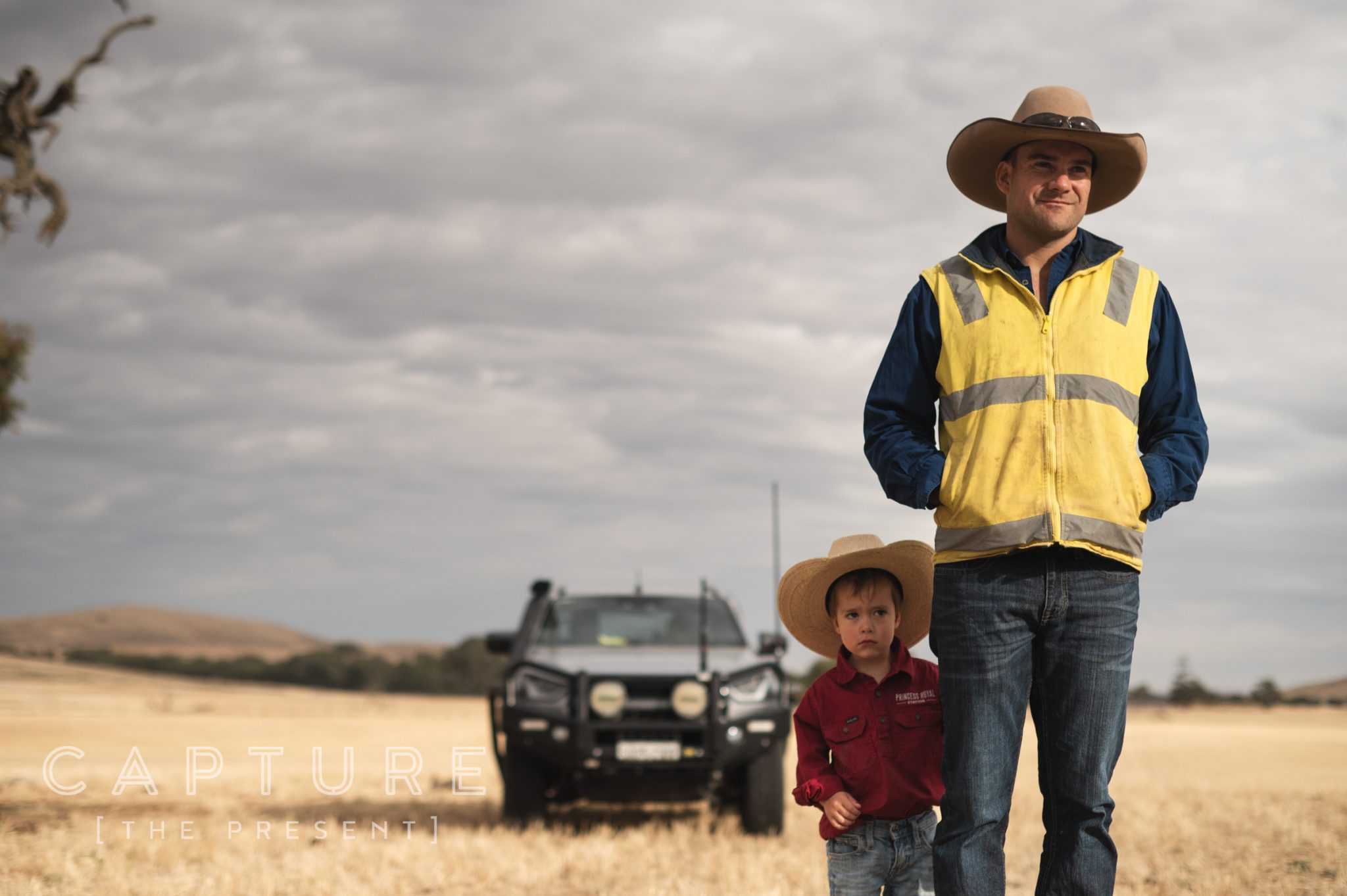 Station worker in high vis standing with a young child beside a ute in stubble