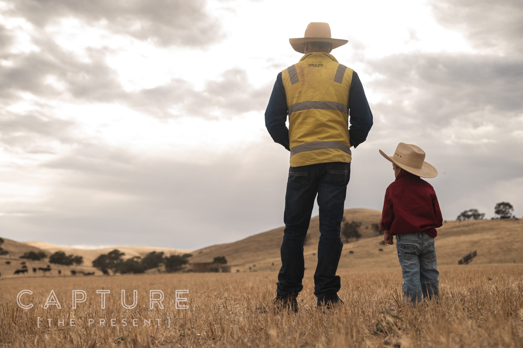 Station worker and a young boy in matching hats looking out over the paddocks