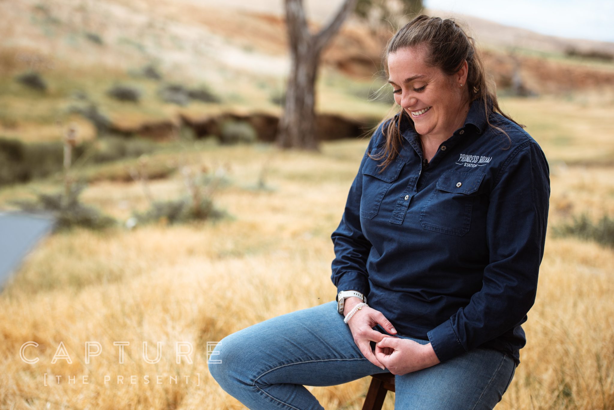 Station worker in a Princess Royal shirt sitting on a stool beside a creek